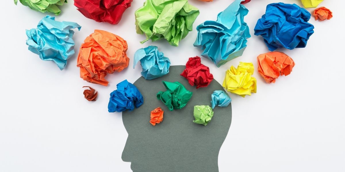 Silueta de cabeza humana con papeles de colores representando la generación de ideas innovadoras y procesos cognitivos.